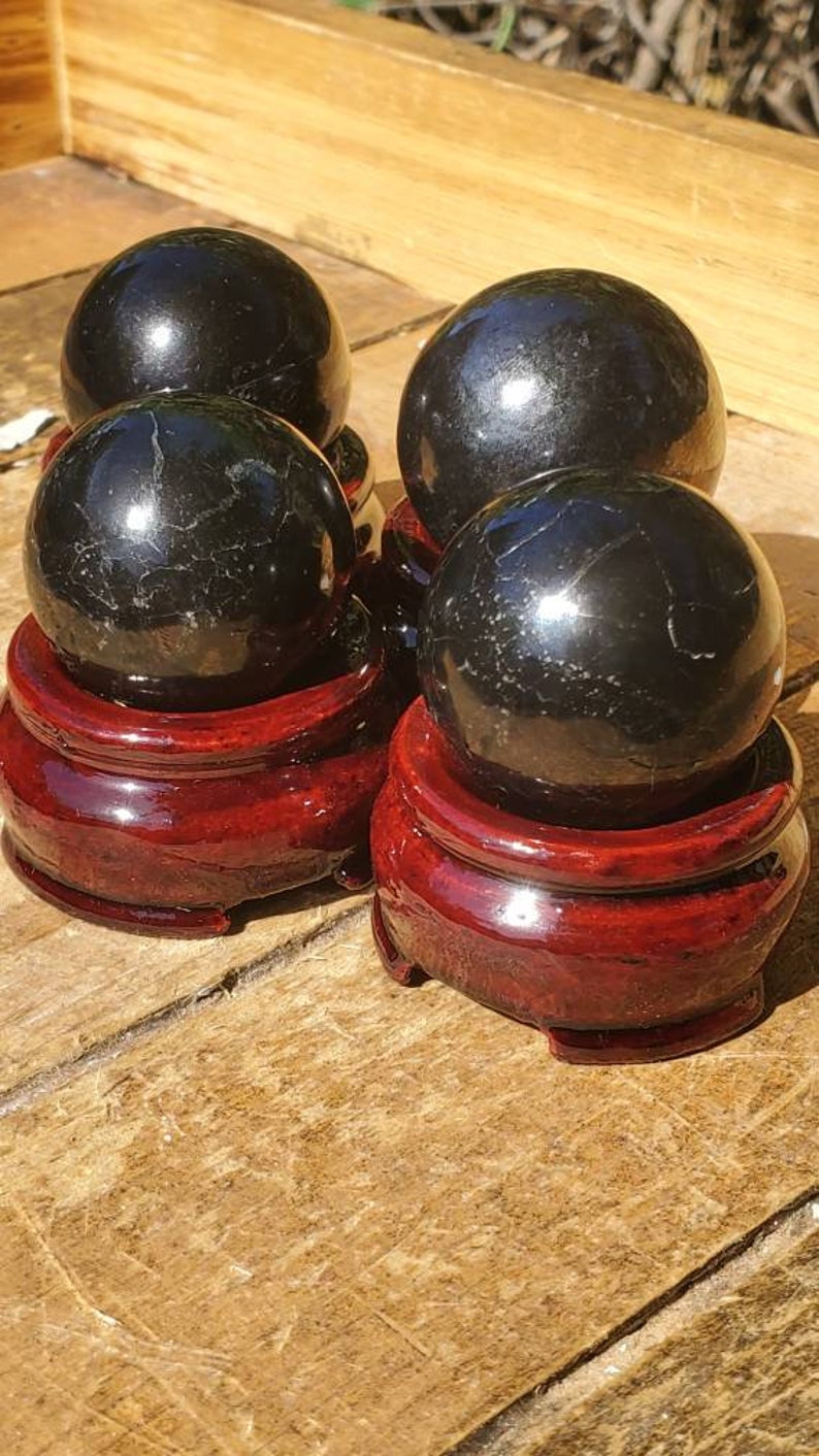 May include: Four black obsidian spheres on red wooden stands. The spheres are polished and reflect light.
