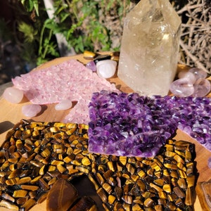 May include: A collection of crystals arranged on a wooden surface. The crystals include a large clear quartz point, a pink rose quartz cluster, a purple amethyst cluster, and a golden tiger's eye cluster.