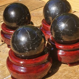 May include: Four black obsidian spheres on red wooden stands. The spheres are polished and reflect light.