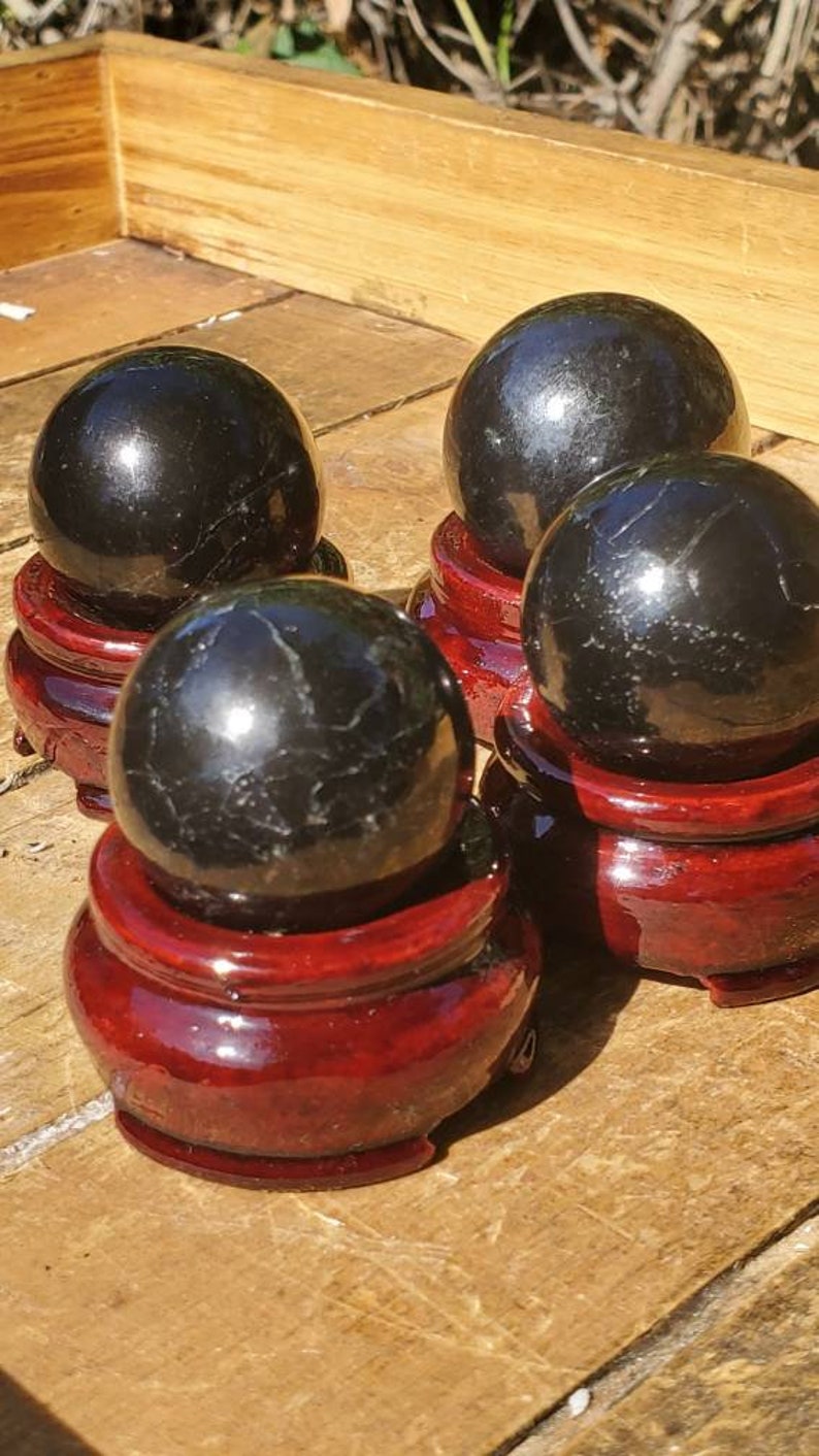 May include: Four black obsidian spheres on red wooden stands. The spheres are polished and reflect light.