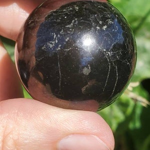 May include: A smooth, black obsidian sphere with a high polish. The sphere has a few natural inclusions and a slight sheen.
