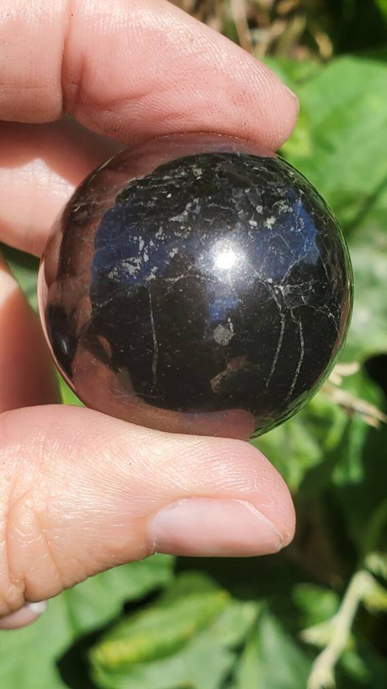 May include: A smooth, black obsidian sphere with a high polish. The sphere has a few natural inclusions and a slight sheen.