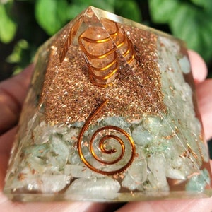 K&ouml;nnte beinhalten: Eine klare Kristallpyramide mit gr&uuml;nen und goldenen Kristallen im Inneren. Die Pyramide hat ein spiralf&ouml;rmiges Design aus Kupferdraht im Inneren.