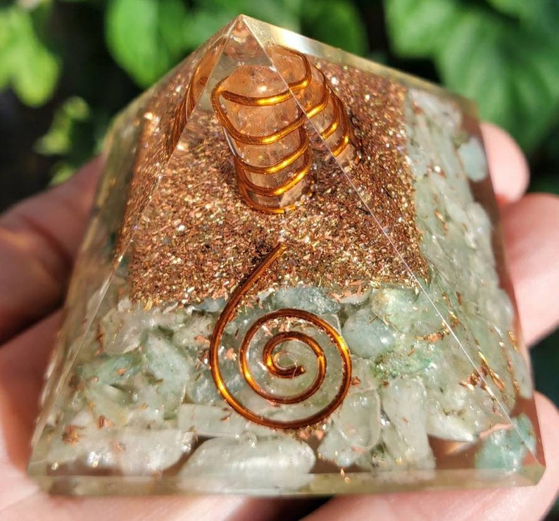 K&ouml;nnte beinhalten: Eine klare Kristallpyramide mit gr&uuml;nen und goldenen Kristallen im Inneren. Die Pyramide hat ein spiralf&ouml;rmiges Design aus Kupferdraht im Inneren.