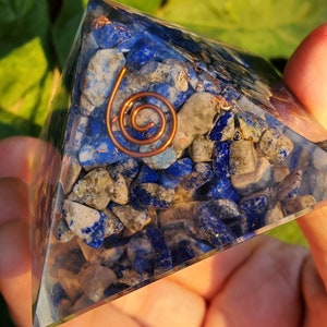 K&ouml;nnte beinhalten: Eine klare Kristallpyramide gef&uuml;llt mit kleinen blauen und grauen Steinen. Eine Kupferspule ist in die Pyramide eingebettet.