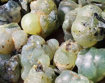 May include: A collection of green and black moss agate stones. The stones are smooth and have a variety of shapes and sizes.
