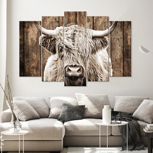 May include: A close-up of a highland cow with long, white fur and a brown wooden background. The cow is looking directly at the camera.