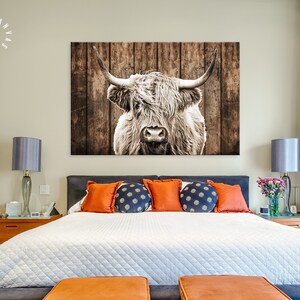 May include: A close-up of a white Highland cow with long, shaggy hair, looking directly at the camera. The cow is in front of a rustic wooden background.
