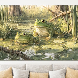 May include: A rectangular wall art print featuring a detailed painting of two green frogs resting in a swampy pond. The scene includes lily pads, tall reeds, and a fallen log in the water, rendered in shades of green, brown, and soft yellow light.