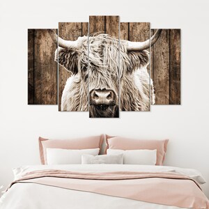 May include: A close-up of a white highland cow with long, shaggy hair. The cow's head is centered in the image, and its eyes are looking directly at the viewer. The background is a rustic wooden wall.