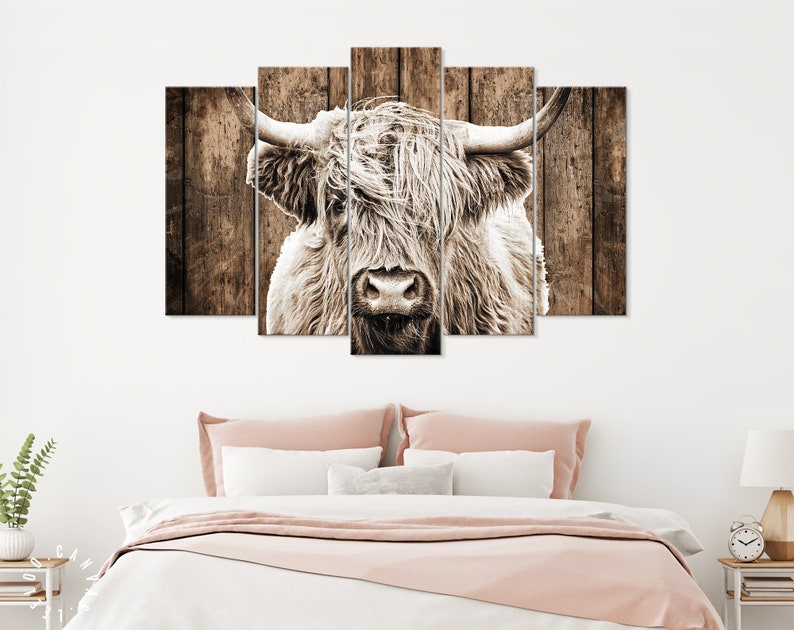 May include: A close-up of a white highland cow with long, shaggy hair. The cow's head is centered in the image, and its eyes are looking directly at the viewer. The background is a rustic wooden wall.