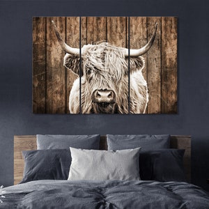 May include: A close-up of a highland cow's face with long, shaggy hair. The cow is looking directly at the camera. The background is a rustic wooden wall.