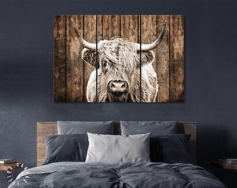 May include: A close-up of a highland cow's face with long, shaggy hair. The cow is looking directly at the camera. The background is a rustic wooden wall.