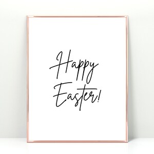 May include: A framed print with a rose gold border. The white background features the words "Happy Easter!" in elegant black script. The artwork is a simple, yet stylish, seasonal decoration.