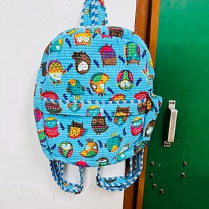 Puede incluir: Una mochila acolchada azul con estampado de b&uacute;hos coloridos. La mochila tiene un asa superior y correas ajustables.