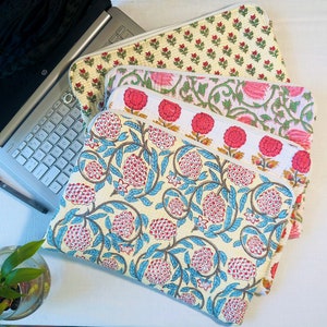 May include: A stack of four laptop sleeves with floral patterns. The sleeves are made of quilted fabric and have a cream background with pink and blue floral designs.