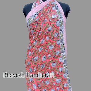 May include: A pink and white cotton sarong with a floral print. The sarong is wrapped around a mannequin and has a halter neck style. The sarong has a white border with a pink and white striped trim.