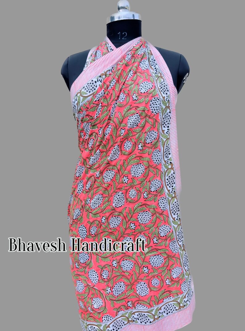 May include: A pink and white cotton sarong with a floral print. The sarong is wrapped around a mannequin and has a halter neck style. The sarong has a white border with a pink and white striped trim.