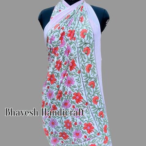 May include: A white cotton sarong with a pink and red floral print. The sarong is tied around a mannequin and has a pink and white striped border.