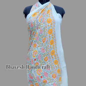 May include: A light blue sarong with a floral print featuring yellow, pink, and green flowers. The sarong is draped over a mannequin and has a white stripe border.