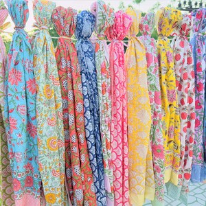 May include: A collection of colourful printed cotton scarves with floral patterns. The scarves are hanging in a row and are all different colours and designs.