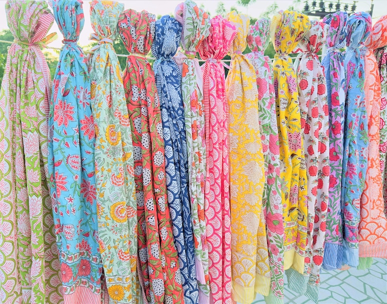 May include: A collection of colourful printed cotton scarves with floral patterns. The scarves are hanging in a row and are all different colours and designs.