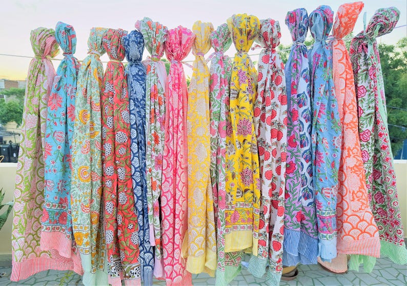 May include: A collection of colourful cotton scarves with floral patterns. The scarves are hanging on a clothesline and are all different colours and designs.