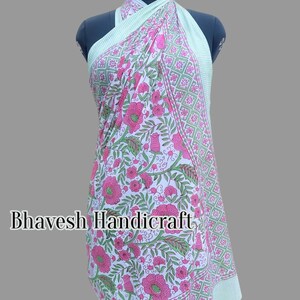 May include: A white cotton sarong with a pink floral print and green geometric border. The sarong is draped over a mannequin and is styled as a dress. The text "Bhavesh Handicraft" is visible on the sarong.