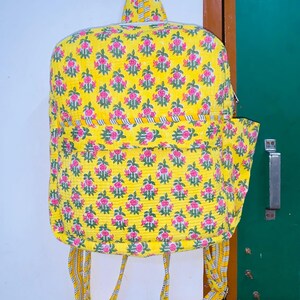 Puede incluir: Una mochila amarilla con estampado floral y correas ajustables. La mochila tiene un peque&ntilde;o bolsillo en la parte delantera y un cierre de cremallera.