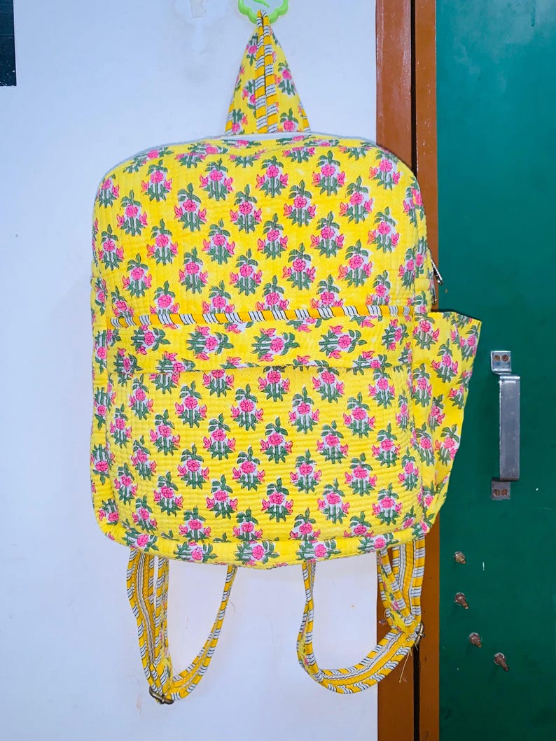 Puede incluir: Una mochila amarilla con estampado floral y correas ajustables. La mochila tiene un peque&ntilde;o bolsillo en la parte delantera y un cierre de cremallera.