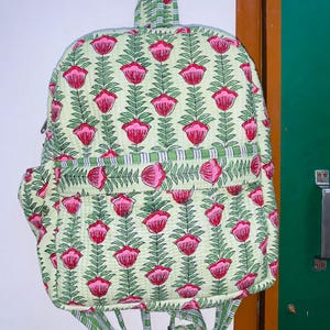 Puede incluir: Una mochila de color verde y rosa con estampado floral, asa superior y correas ajustables.