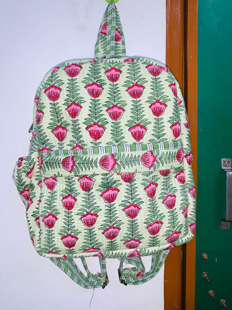 Puede incluir: Una mochila de color verde y rosa con estampado floral, asa superior y correas ajustables.