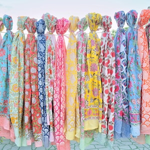 May include: A collection of colourful cotton scarves with floral patterns. The scarves are hanging on a clothesline and are all different colours and designs.