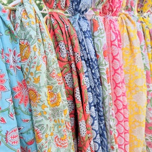 May include: A collection of colourful fabric scarves with floral patterns. The scarves are hanging on a clothesline and are made of a soft, lightweight material.