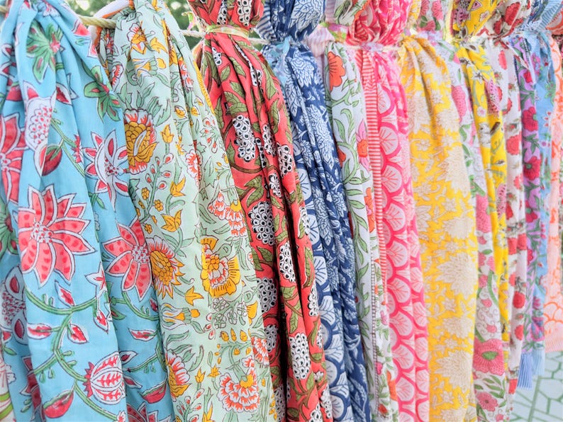 May include: A collection of colourful fabric scarves with floral patterns. The scarves are hanging on a clothesline and are made of a soft, lightweight material.