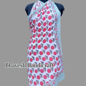 May include: White cotton sarong with a red and green floral print. The sarong is tied around a mannequin and has a halter neck style.