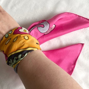 May include: A pink and yellow patterned silk scarf tied around a wrist as a bracelet.