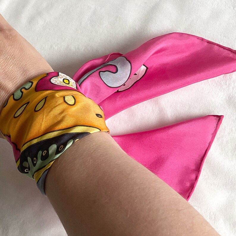 May include: A pink and yellow patterned silk scarf tied around a wrist as a bracelet.