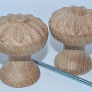 Pode incluir: Dois botões de madeira com um design de flor. Os botões são de cor castanho claro e têm um acabamento liso. Eles são presos a um parafuso de metal.