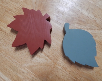 May include: Two wooden leaf-shaped ornaments. One is a red maple leaf and the other is a blue leaf.