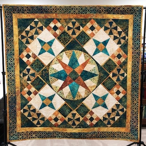May include: A quilt with a geometric pattern in shades of teal, brown, and white. The quilt is framed with a border of gold and green.
