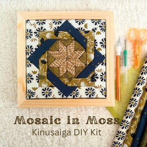 May include: A Kinusaiga DIY kit featuring a square wooden frame containing a fabric mosaic with a star pattern in olive, navy, and white floral prints. Includes a craft knife, seam ripper, orange scissors, and fabric strips labeled Mosaic in Moss.