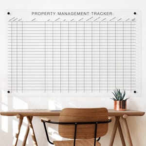 May include: A clear acrylic wall-mounted property management tracker board featuring a black grid and printed headers including lease status, address, rent, and utilities. The rectangular board is secured with four black circular corner mounts.