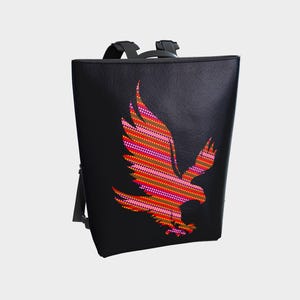 May include: Black leather backpack featuring a red, orange and pink eagle design.