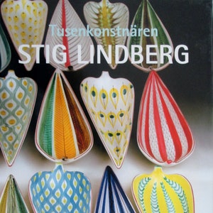 Puede incluir: Una portada de libro con el nombre "STIG LINDBERG" en letras blancas. La portada muestra una colección de piezas de cerámica coloridas en forma de lágrima con varios patrones, incluyendo rayas, diamantes y diseños en forma de plumas. El libro se titula "Tusenkonstnären".
