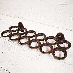 Könnte beinhalten: Ein rustikaler brauner Handtuchhalter aus Metall mit 14 runden Haken. Der Halter ist an einer weißen Holzwand montiert.