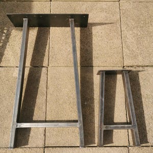 May include: Two metal table legs, one taller than the other, with a flat top. The legs are made of sturdy metal and have a simple, industrial design.