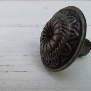 Peut inclure: Un bouton de porte en métal argenté avec un motif floral décoratif. Le bouton a une base ronde et un motif circulaire surélevé au centre.