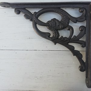 Puede incluir: Soporte de estante de hierro fundido negro con un diseño decorativo que presenta un pez estilizado y motivos florales.