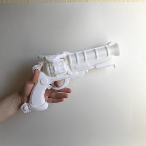 以下が含まれることがあります： シンプルな背景に、詳細な装飾が施された白いおもちゃの銃。おもちゃの銃は、ヴィンテージのリボルバーに似た、詳細なバレル、トリガー、ハンドルを備えています。全体的なデザインは、すっきりとしたモノクロです。